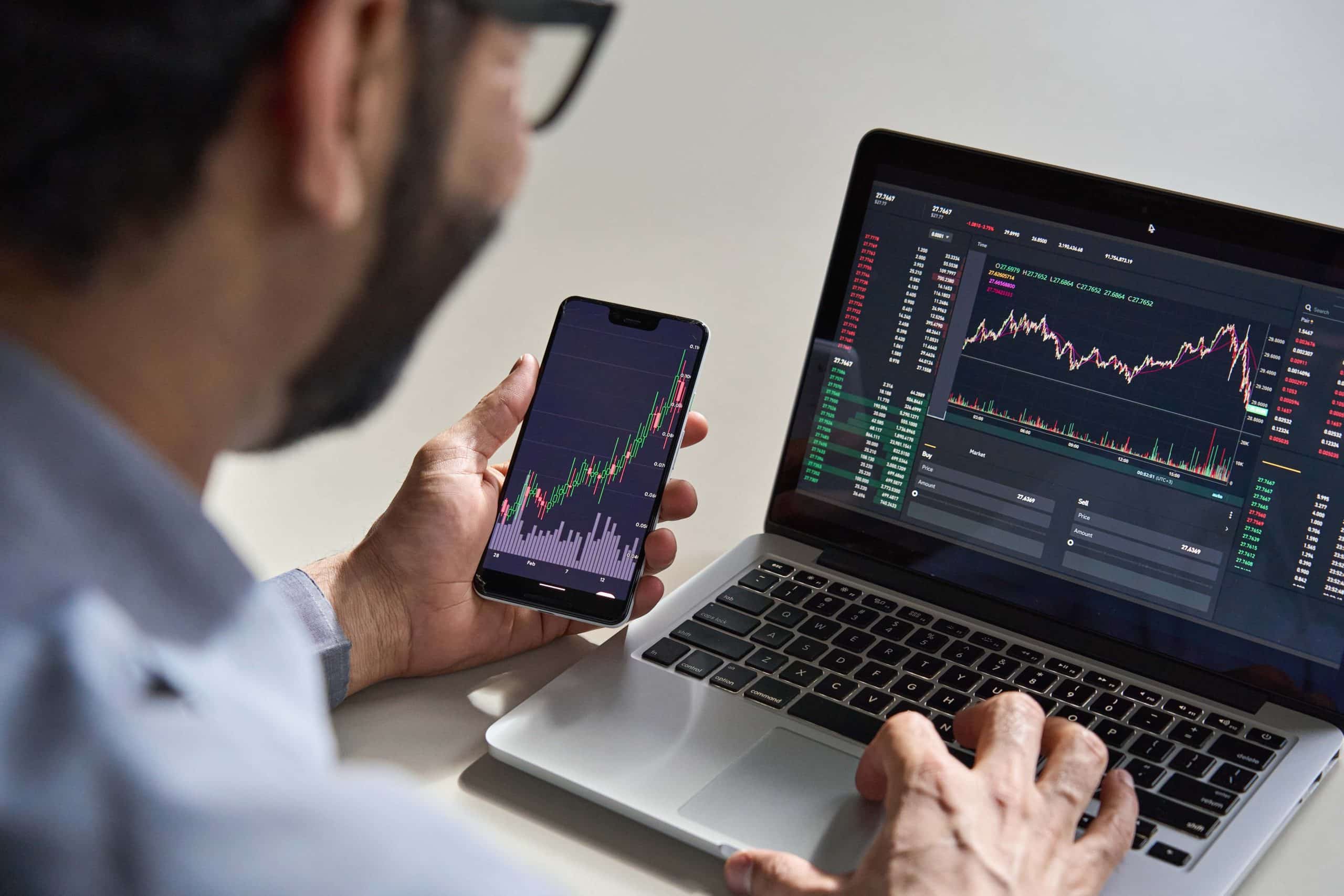 Man trading on laptop and phone